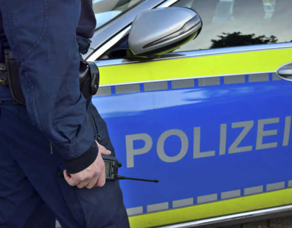 Ein Polizist neben einem deutschen Polizeiauto mit einem Handy in der Hand ©panthermedia