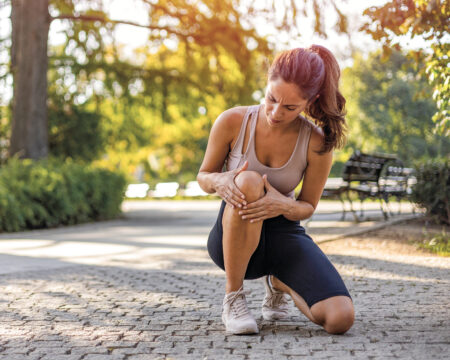 Frau hält sich nach Joggen im Wald das Knie. Symbolbild Sportverletzung für Advertorial Sander Apotheken. ©Dragana Gordic/stock.adobe.com