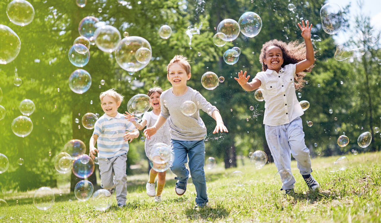 Symbolbild Kindergeburtstag. Kinder spielen draußen mit Seifenblasen.
