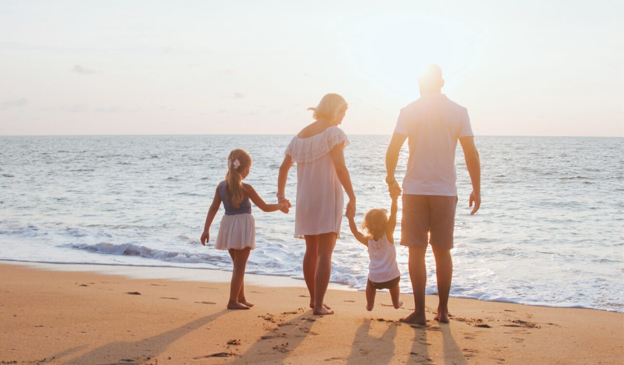 Eine Familie mit zwei kleinen Kindern steht barfuß am Sandstrand