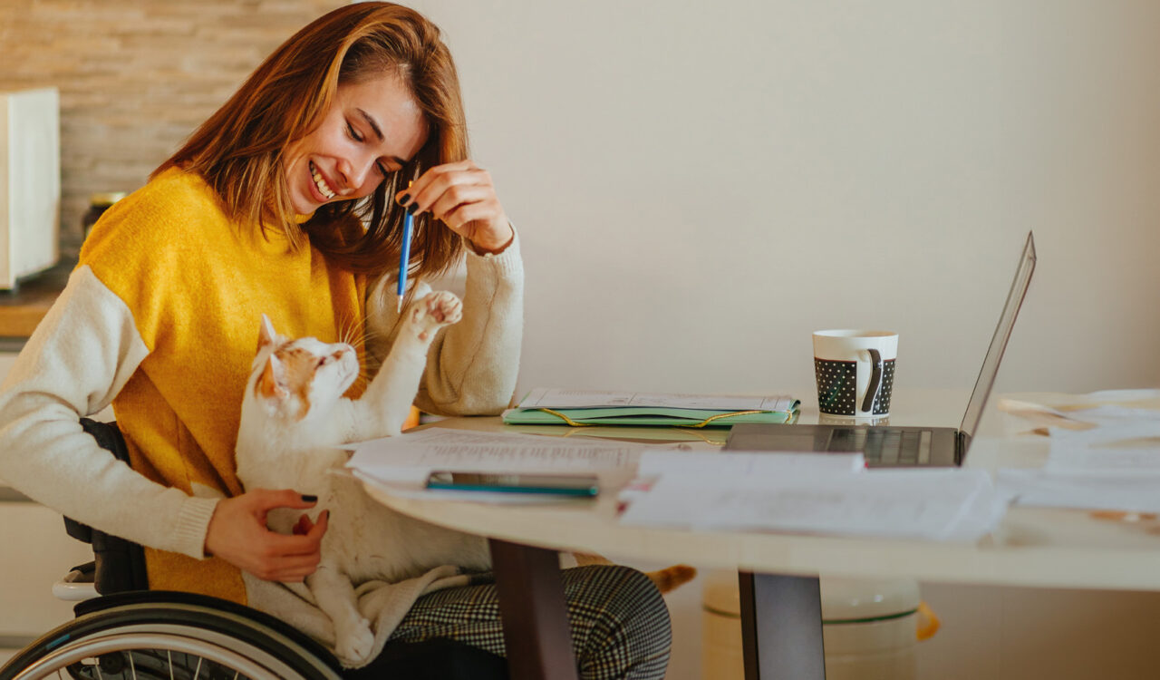 Eine junge Frau im Rollstuhl spielt mit ihrer Katze