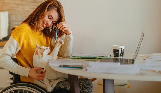 Eine junge Frau im Rollstuhl spielt mit ihrer Katze